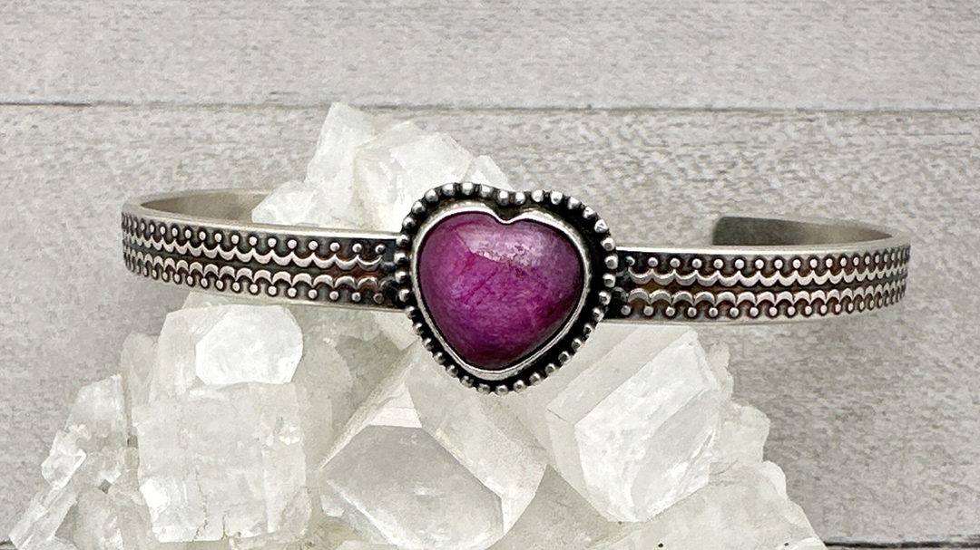 Pink heart shaped ruby and sterling silver cuff bracelet sitting on white crystals. 