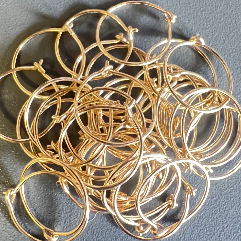 a pile of 14k yellow gold fill hoop earrings on a gray background