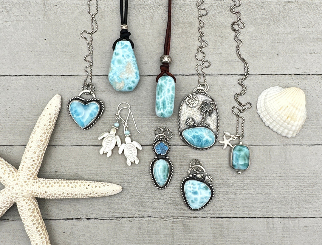 picture of 8 jewelry pieces of larimar on a gray background with shell and starfish off to the side. 